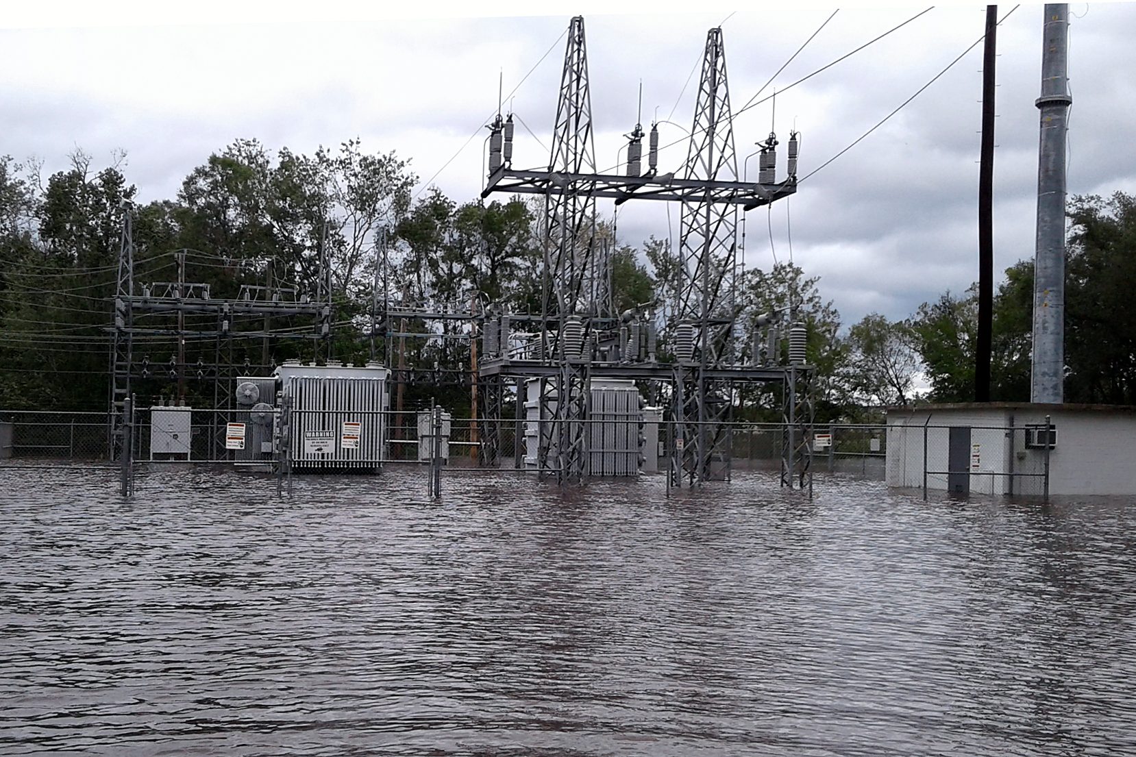 Brown floodwater surrounding an electrical substation held back by a barrier ring