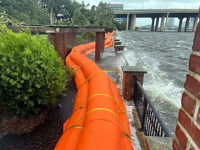 Wind-driven river water breaking in whitecaps against a brick seawall below a barrier line