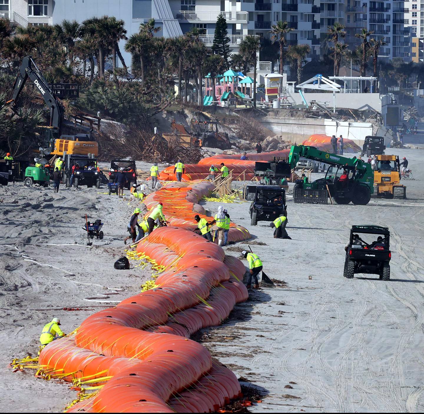 Crew installing a long water-filled barrier along an oceanfront beach below eroded dunes