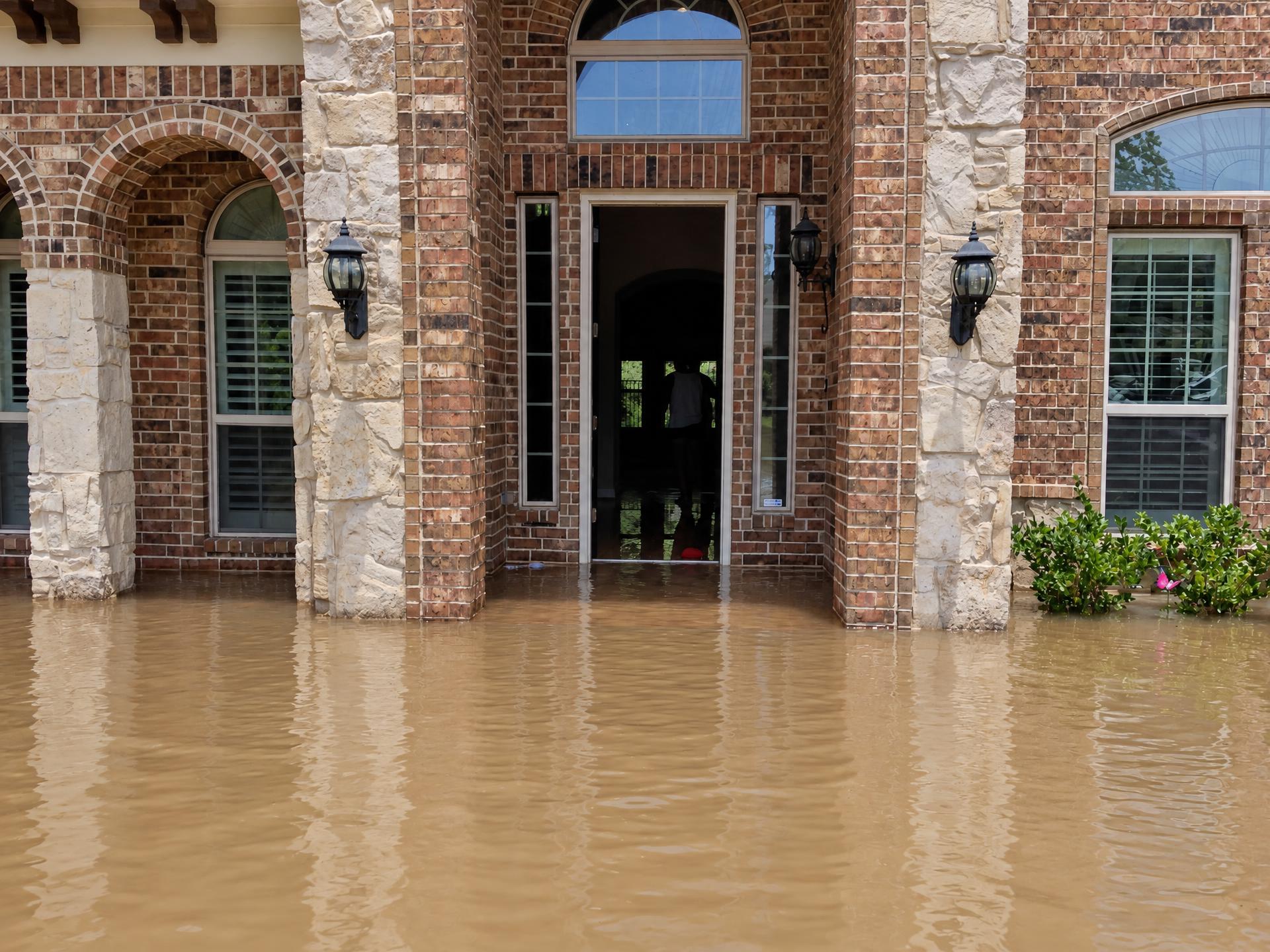 Brown floodwater filling a home's covered front entryway up to the door threshold
