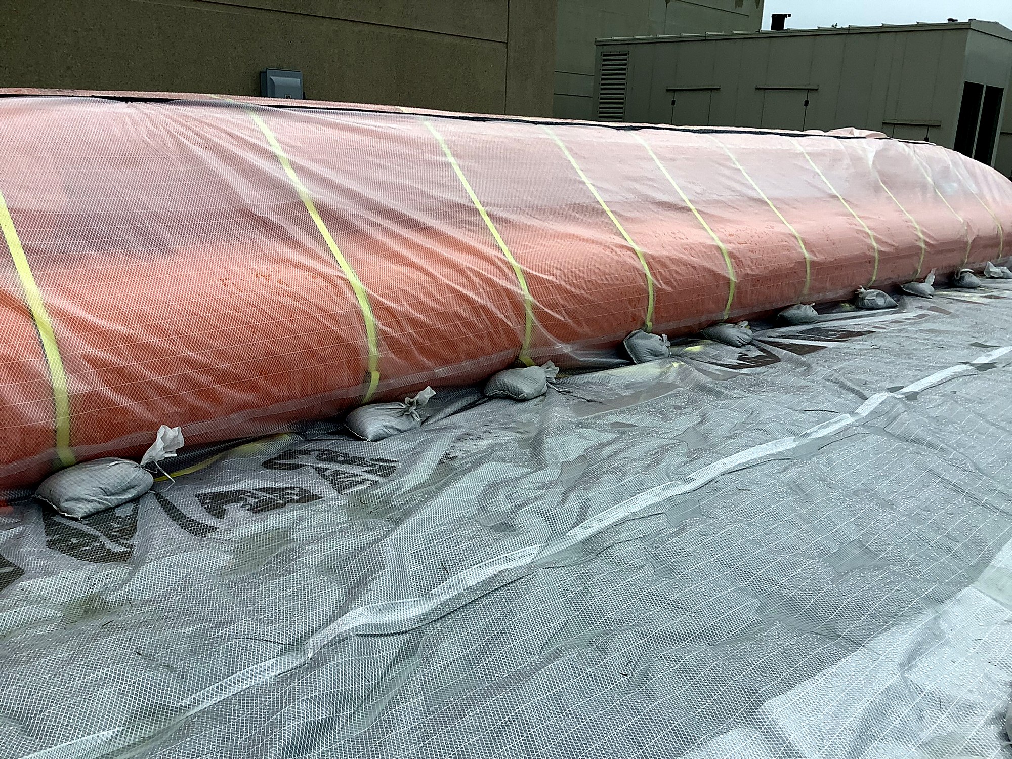 Water-filled barrier tube with clear sheeting and sandbags set along a hospital foundation wall
