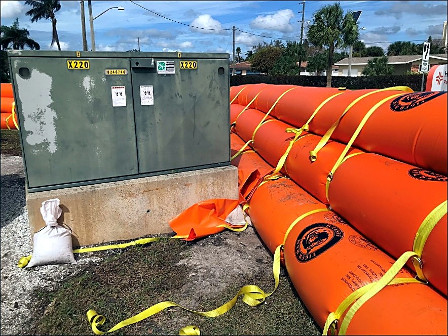 Orange water-filled barrier tubes forming a closed ring around a pad-mounted electrical transformer