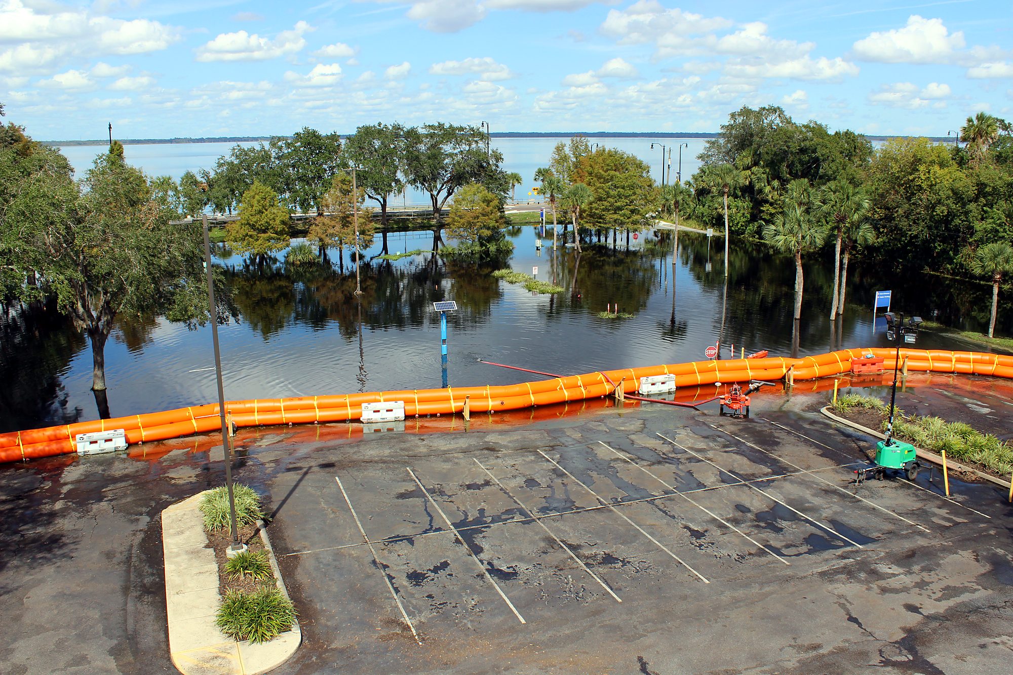 Water-filled barrier line separating a dry hospital parking lot from lakefront floodwater