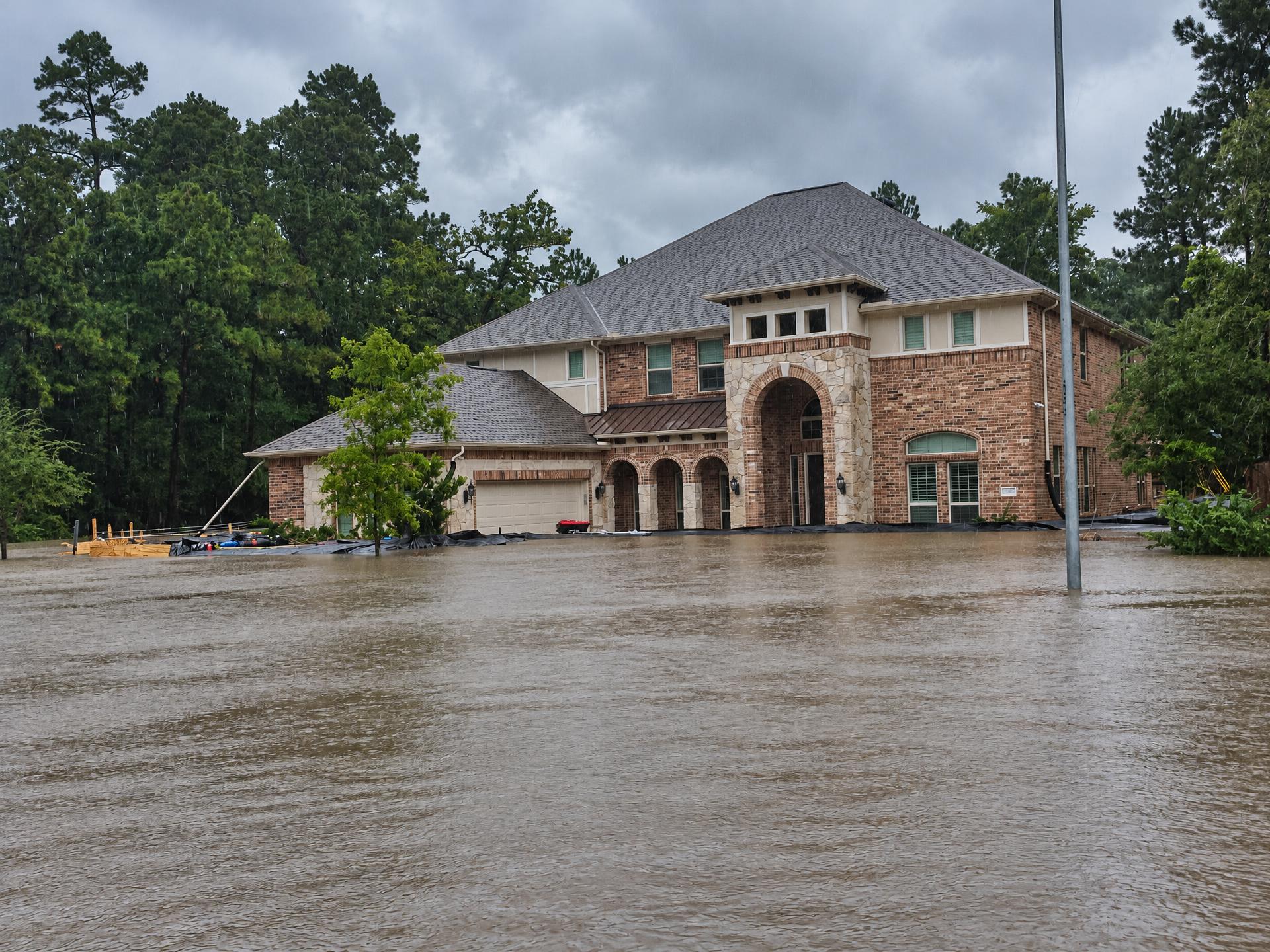 A brick home in heavy rain with floodwater across the front lawn and driveway