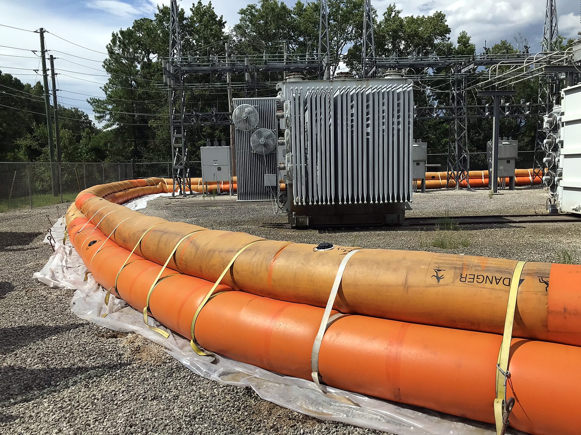 Stacked orange water-filled barrier tubes running in a line across a substation site